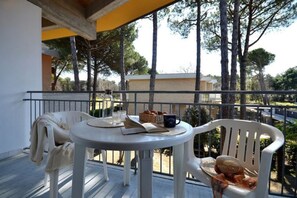 A balcony with a round table, two chairs, a book, a basket of bread, and a mug.