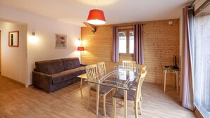 Een gezellige woonkamer met een eettafel met glazen blad, houten stoelen, een bruine bank en een rode hanglamp.