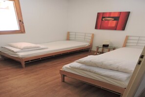 Two single beds with wooden frames and white bedding in a room with wooden flooring and a window. - Attractive apartment in Orelle for family (Orelle)