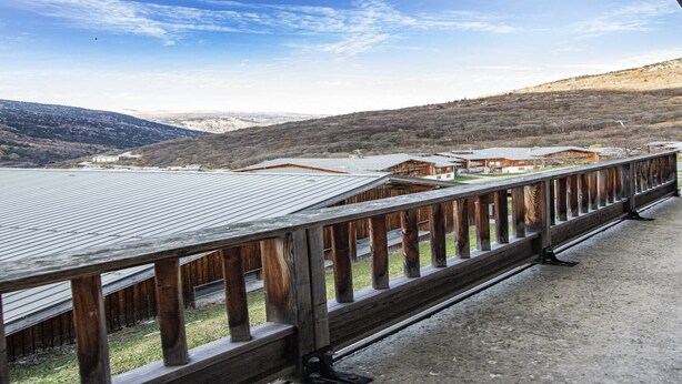 Een houten balkon met uitzicht op een bergachtig landschap en verschillende gebouwen.
