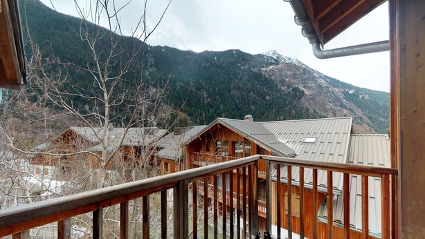 A wooden cabin with a balcony, surrounded by mountains and trees. - Apartment in Orelle with ski storage (Orelle)
