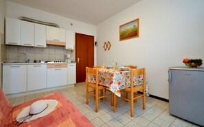Uma cozinha compacta com armários brancos, uma mesa de jantar com toalha de mesa florida e uma geladeira.