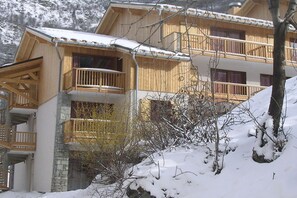 A wooden chalet with balconies, stone foundation, and snow-covered surroundings.