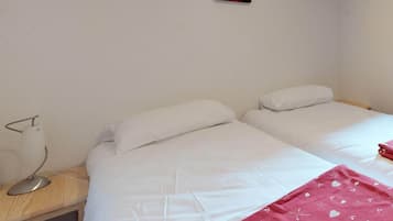 A simple, clean room with two single beds, a bedside table with a lamp, and a small red decoration on the wall.