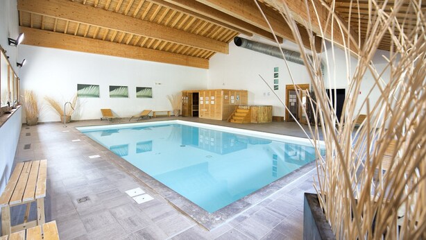 Una piscina con vigas de madera, zona de estar y sauna.