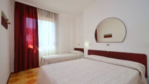 Une chambre d’hôtel avec deux lits, une grande fenêtre avec des rideaux, un miroir rond accroché au mur et un plancher en bois.