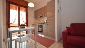Une cuisine moderne avec des meubles en bois, un coin repas avec une table et des chaises blanches, et un canapé rouge dans l’espace salon.