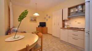 Eine kompakte Küche mit Essbereich, ausgestattet mit einem runden Holztisch, Stühlen, einem Fernseher, Schränken und einem Kühlschrank.