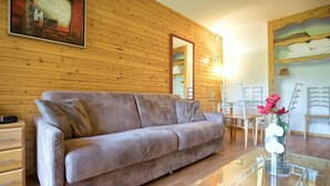 Ein modernes Wohnzimmer mit Sofa, Glastisch, Holzwänden und einem Gemälde.