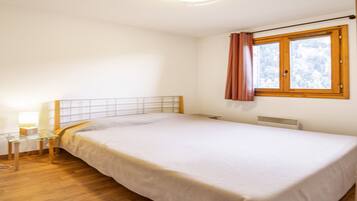 Une chambre avec un lit simple, une table de chevet avec une lampe, une fenêtre avec des rideaux et un radiateur.