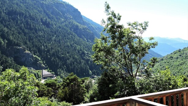 Paisagem montanhosa com florestas densas e um edifício com telhado inclinado.