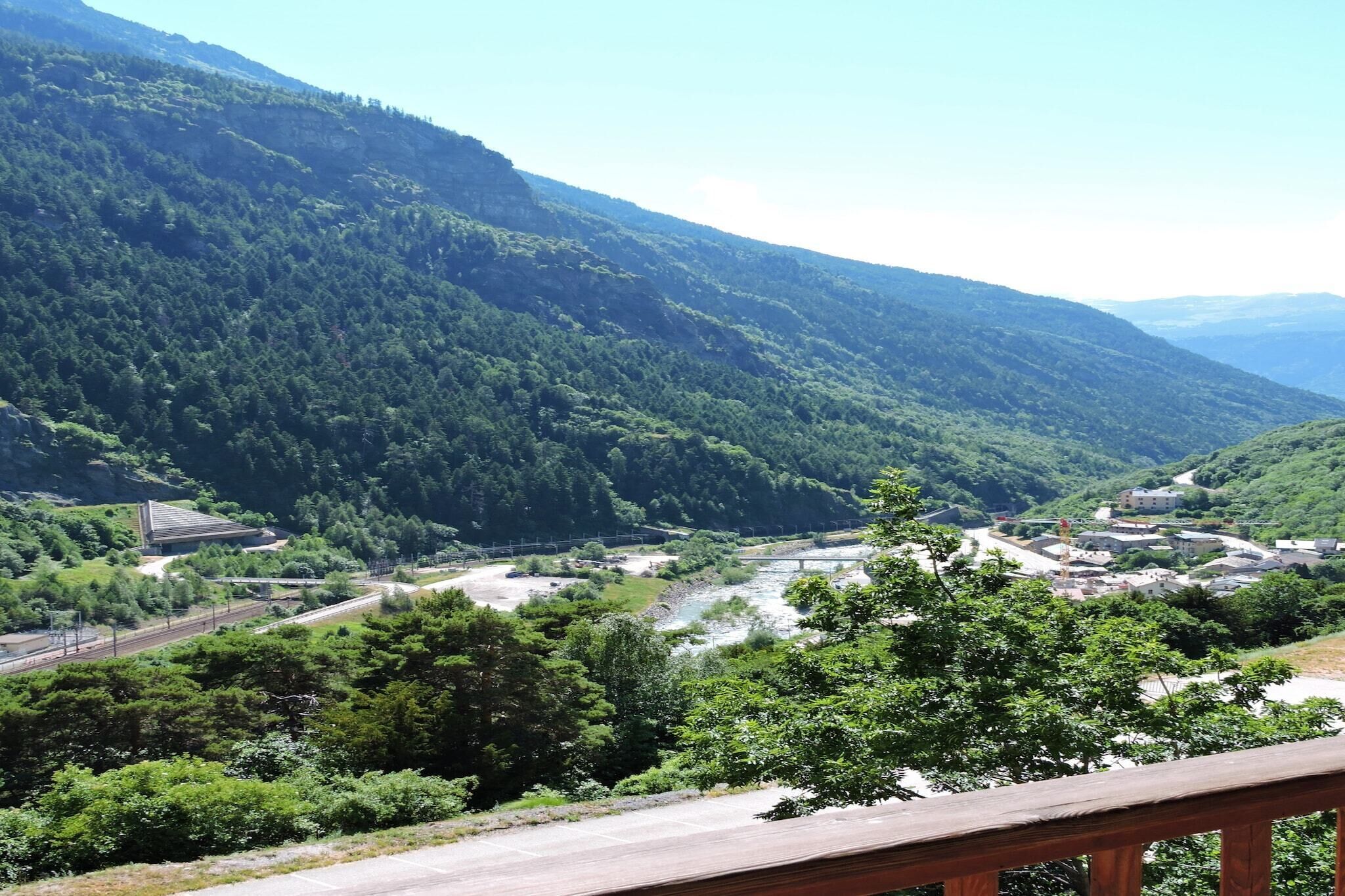 Eine gebirgige Landschaft mit einem Fluss, einer Brücke und einer kleinen Siedlung mit Gebäuden.
