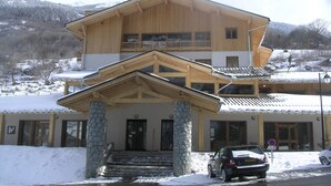 Un edificio de madera de dos pisos con entrada de piedra y un balcón en el nivel superior.