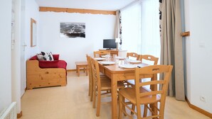 A dining area with a wooden table and chairs, a television, and a red sofa.