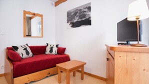 A cozy room with a red sofa, a wooden table, a TV, and a mirror on the wall.