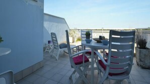 Une terrasse sur le toit, avec des chaises blanches et une table, un pot de fleurs et une vue sur le ciel.