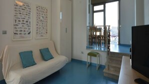 Un salon avec un canapé, une petite table et un téléviseur. Deux affiches représentant des poissons, encadrées, sont accrochées au mur.