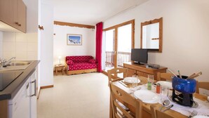 A compact kitchen with a dining area, a red sofa, and a TV.
