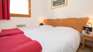 A bedroom with a wooden headboard, a window with a red curtain, a bedside table with a lamp, and a framed picture on the wall.