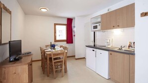A compact kitchen with wooden cabinets, a microwave, a sink, and a dining area with a table and chairs.