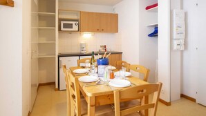 A compact kitchen with wooden cabinets, a microwave, and a small dining table set for four. - Apartment in Val Cenis near River (Val Cenis)