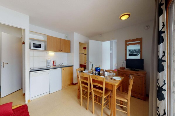 A compact kitchen with white cabinets, a microwave, a sink, and a dining area with wooden chairs and a table. - Apartment in Val Cenis near Ski area (Val Cenis)