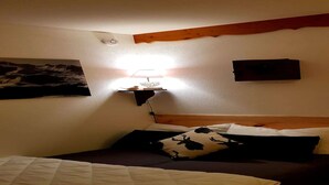 Une chambre à coucher avec un lit, une table de chevet avec une lampe, un tableau au mur et une poutre en bois au-dessus du lit.