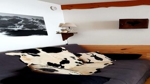 Une chambre à coucher avec un lit, une lampe fixée au mur, un tableau encadré et une poutre en bois au-dessus du lit.