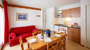 Un espacio habitable compacto con comedor, un sofá rojo, una mesa de madera preparada para dos comensales y una kitchenette.