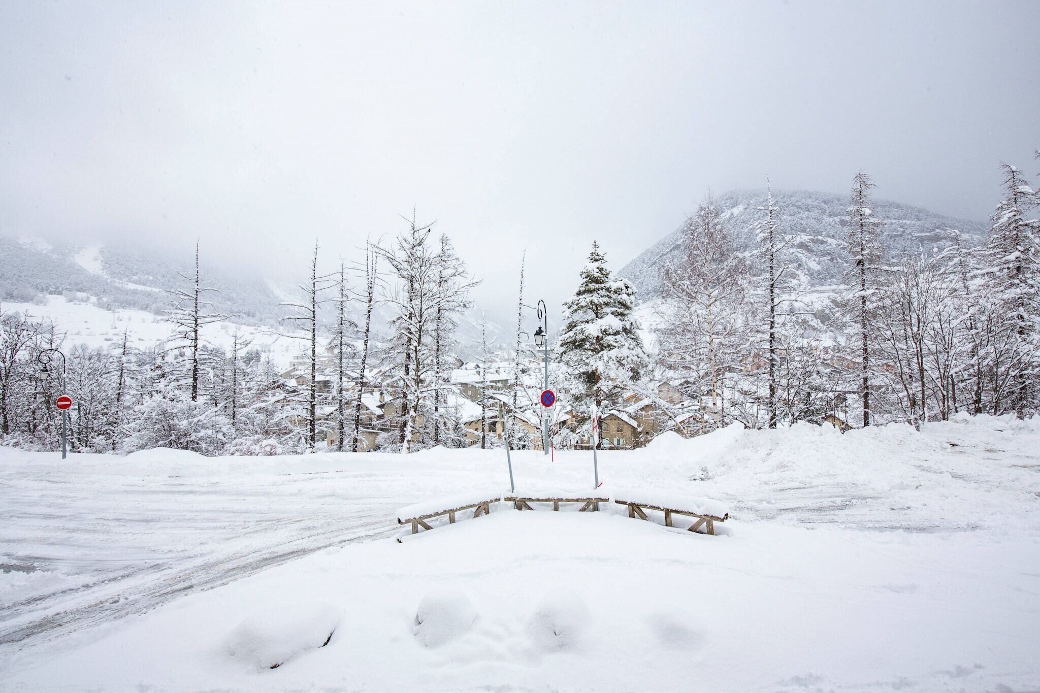 A snow-covered landscape with a road, a wooden fence, and a mountain in the background.