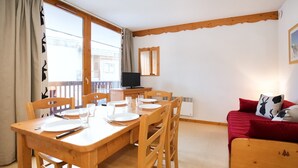 A dining area with a wooden table set for four, a red sofa, and a television on a stand. - Apartment with 2 rooms, balcony (Val Cenis)