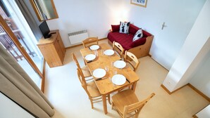 A dining area with a wooden table set for four, a red sofa, and a television on a wooden cabinet. - Apartment with 2 rooms, balcony (Val Cenis)