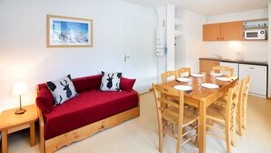 A compact living space with a wooden sofa, a dining table set for four, and a kitchenette with a microwave. - Apartment with 2 rooms, balcony (Val Cenis)