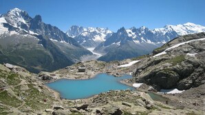 Un paisaje montañoso con un lago azul cristalino, terreno rocoso y picos nevados al fondo.