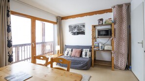 Una habitación acogedora con una mesa de comedor de madera, un sofá con cojines estampados, un estante para microondas y vistas a través de un ventanal grande.