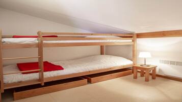Een stapelbed met opbergladen, een tafeltje met een lamp en een radiator aan de muur.