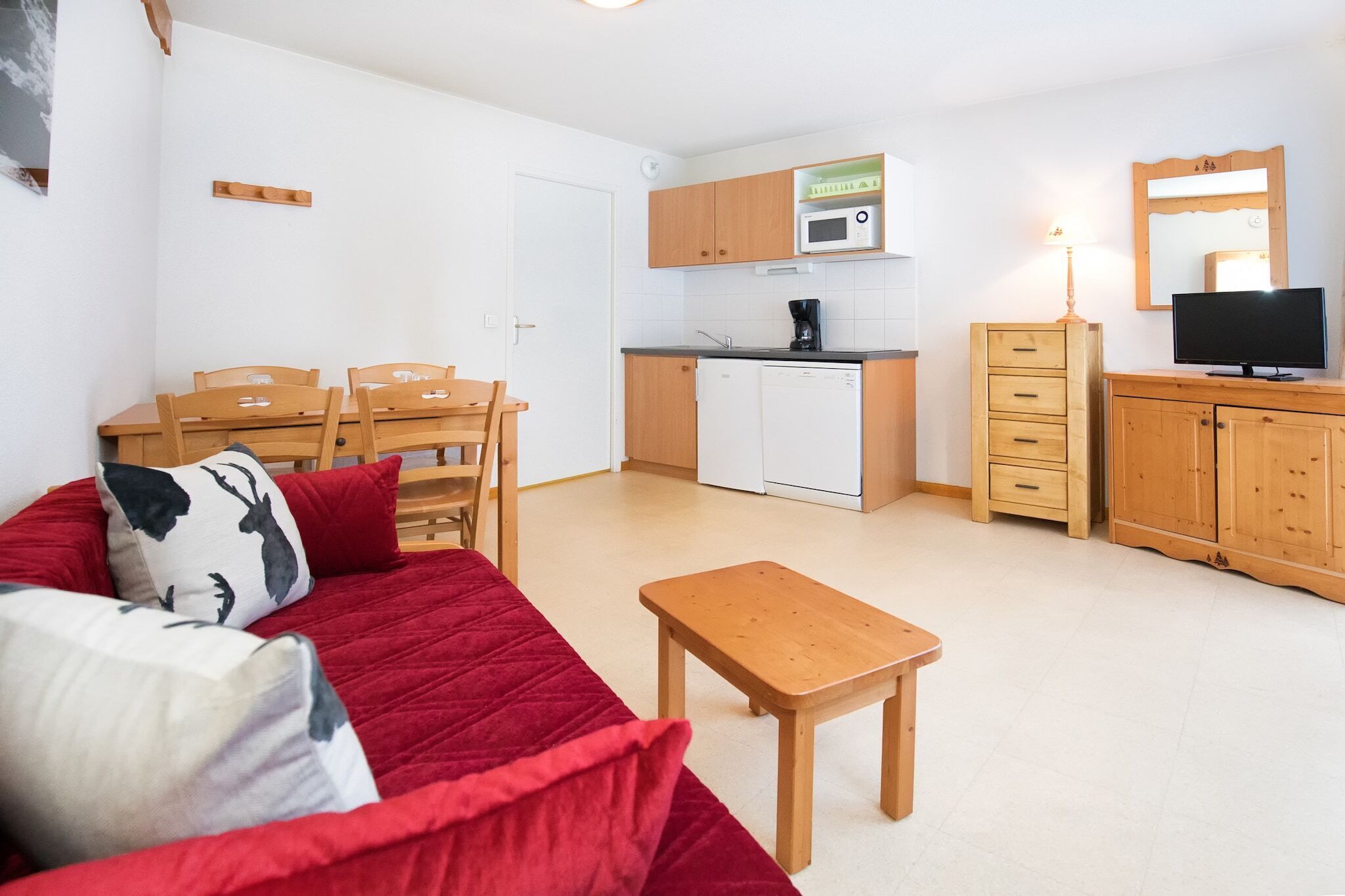 Ein kompakter Wohnraum mit Küchenzeile, Essbereich und Sitzgruppe mit rotem Sofa und Holzmöbeln.