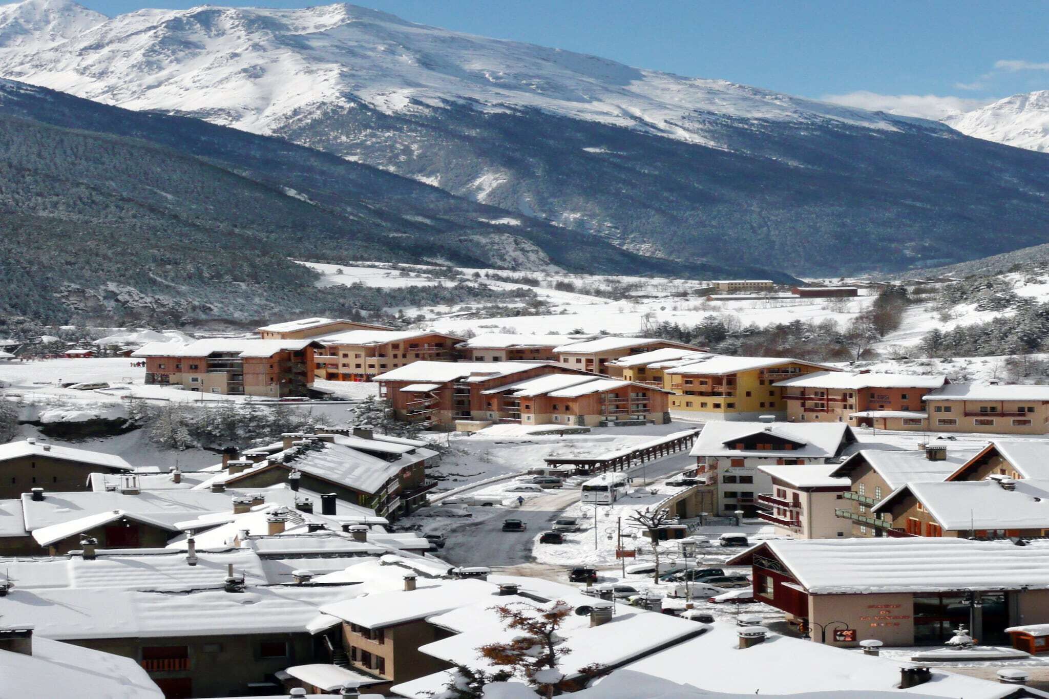 A snow-covered town with buildings, including a hotel with multiple floors and a ski lift visible in the background.