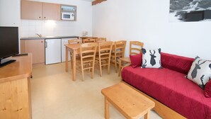 Een ruimtelijk ingerichte leefruimte met een kitchenette, een eethoek en een rode bank met decoratieve kussens.
