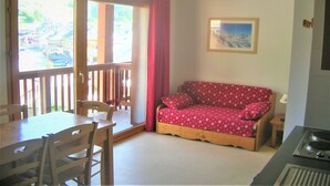 Een kamer met een houten eettafel, stoelen, een rode bank, een schilderij aan de muur en uitzicht door een deur.