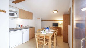 Een kleine keuken met witte apparaten, houten kastjes en een eethoek met een tafel voor vier personen.