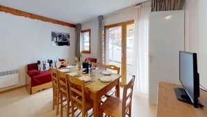 Ett mysigt rum med ett matbord för fyra personer, en soffa, en tv och ett fönster med gardiner.