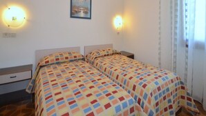 A room with two beds, each with a patterned bedspread, a nightstand, a drawer, and a wall-mounted picture.