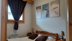 Een slaapkamer met een bed, twee nachtkastjes met lampen, een raam met gordijnen, en drie aan de muur bevestigde afbeeldingen van bergen en een skilift.