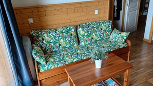 Een houten bank met een tropisch printje, een houten bijzettafeltje met een potplant en een tijdschrift op tafel.