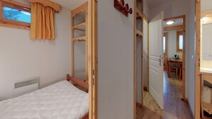 Un dormitorio con estructura de cama de madera, una ventana con cortina, un radiador y una puerta de madera que da a una zona de cocina.