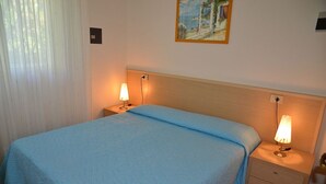 A neatly made bed with a blue blanket, two bedside lamps, and a painting on the wall. - Charming holiday home just steps from the beach (Bibione Pineda)