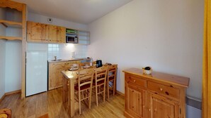 Ett kompakt kök med träskåp, en mikrovågsugn, ett kylskåp och ett matbord med stolar.