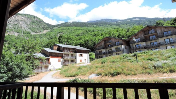 A mountain lodge with a wooden deck and a view of the surrounding forest and hills.