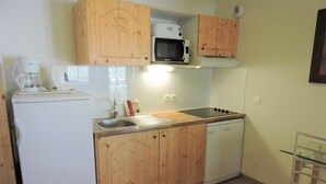 A compact kitchen with wooden cabinets, a microwave, a coffee maker, and a dishwasher.